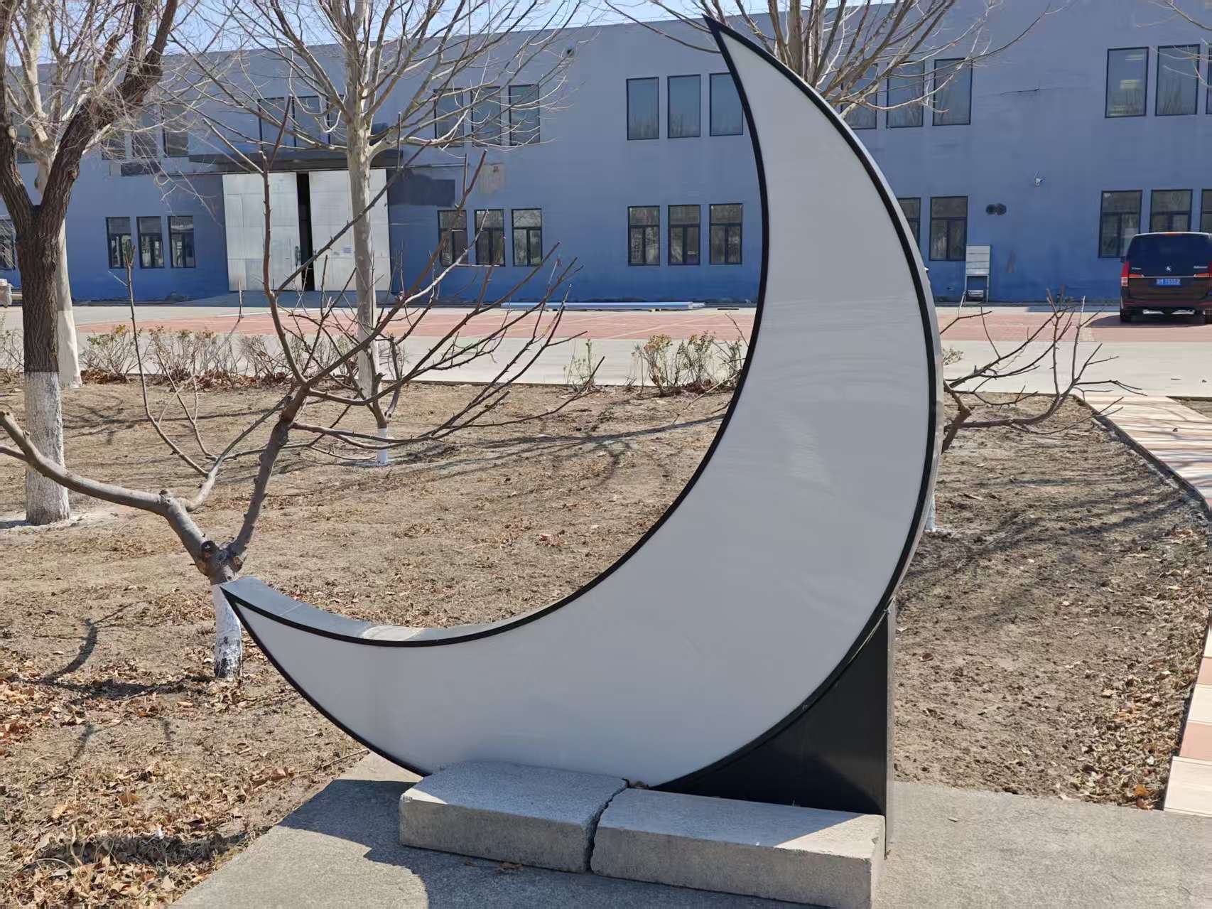 这是一座月牙造型的户外景观装置，以黑白配色勾勒出弯月轮廓，白色发光面板搭配黑色金属边框，底部由水泥块稳固支撑，简约现代又富有诗意，为园区增添了浪漫的艺术氛围。